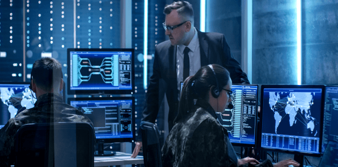 a person in a suit and tie standing in front of a group of people working on computers