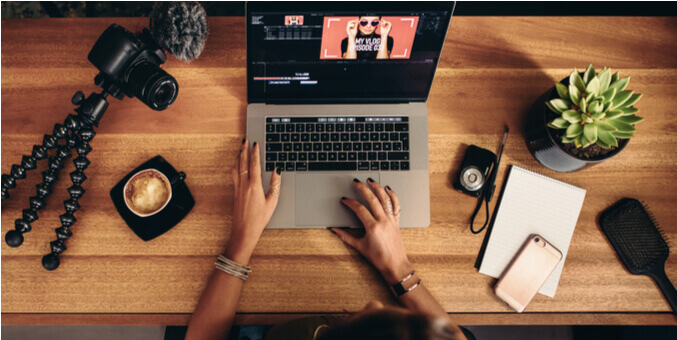 a person's hands on a desk with a laptop and a plant